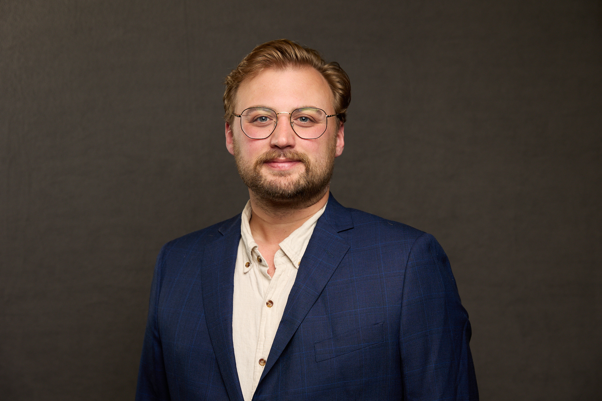 Portrait of author Danny O'Dea, wearing glasses and a navy plaid blazer